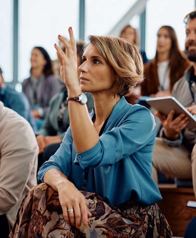 Kobieta siedząca na sali wykładowej z podniesioną do góry ręką